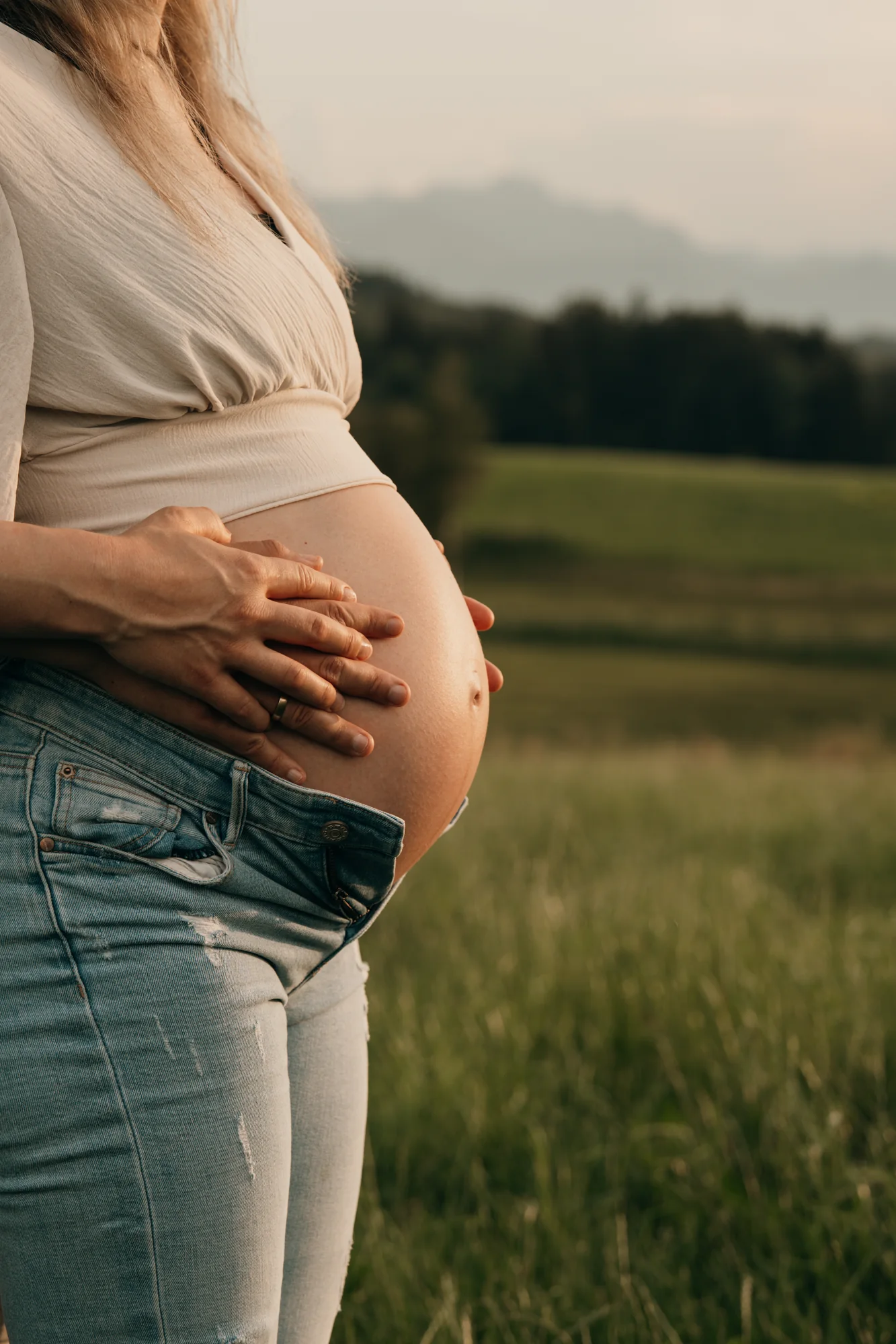 Babybauch im Abendlicht – zwei Hände auf dem Bauch vor der Chiemgauer Landschaft